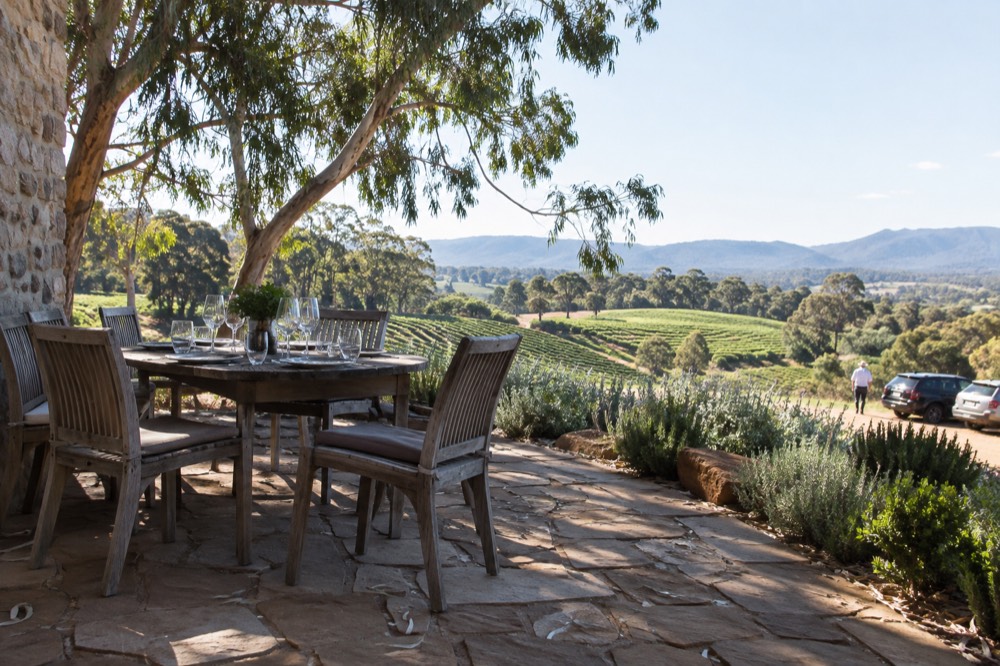 Outdoor dining table with wine glasses overlooking a valley floor vineyard