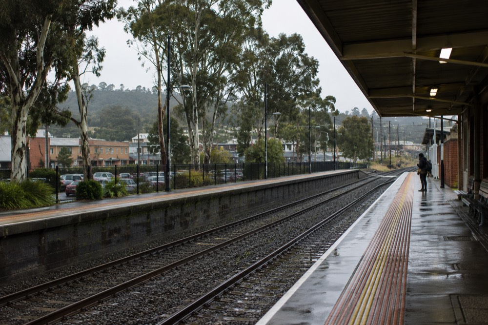 A country railway platform with gum trees and a small township beyond the tracks