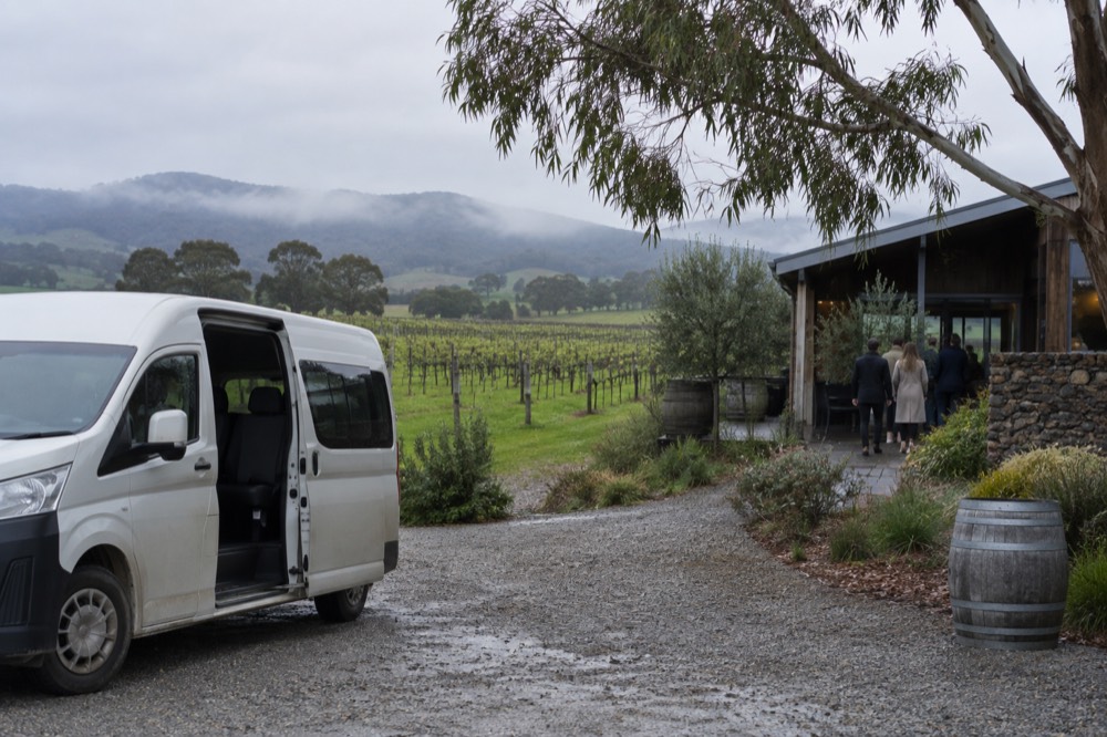 A small tour van parked on a gravel driveway beside a vineyard cellar door