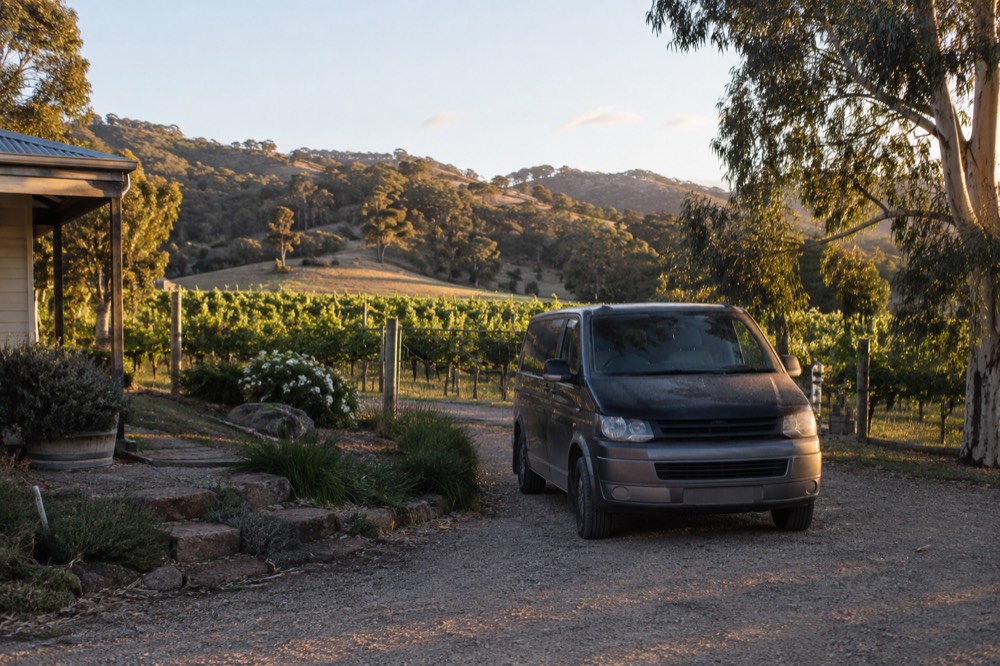 A private van waiting on a winery driveway with rows of vines behind it