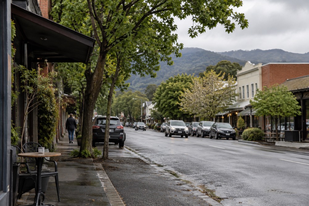 Shopfronts along a tree-lined country main street with hills in the distance