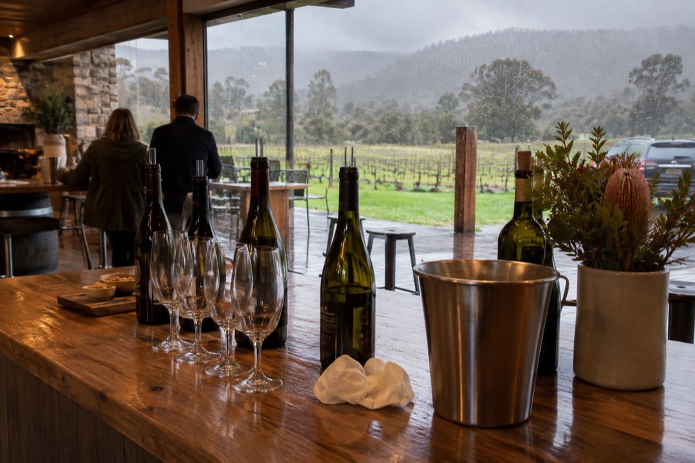 A wooden cellar door tasting counter with wine glasses lined up beside open bottles