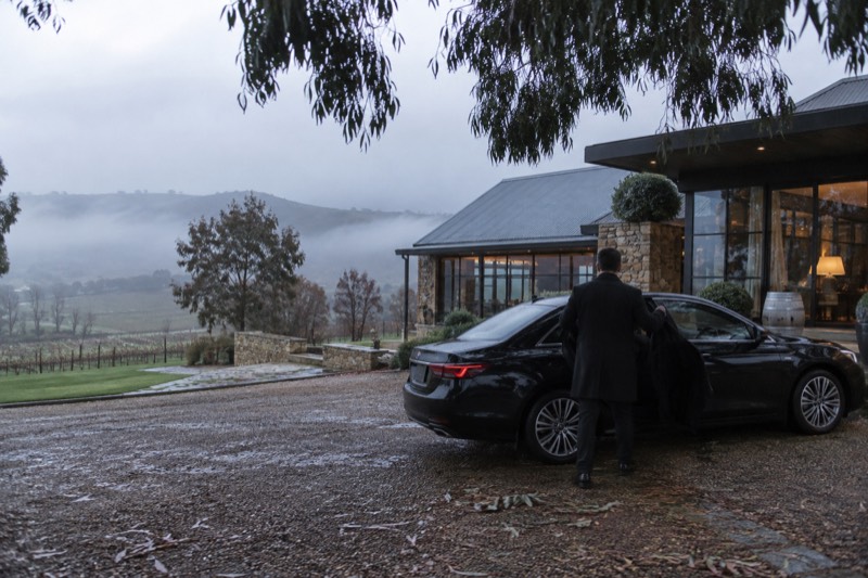Black sedan parked before a stone-and-glass cellar door, morning fog thinning over the valley