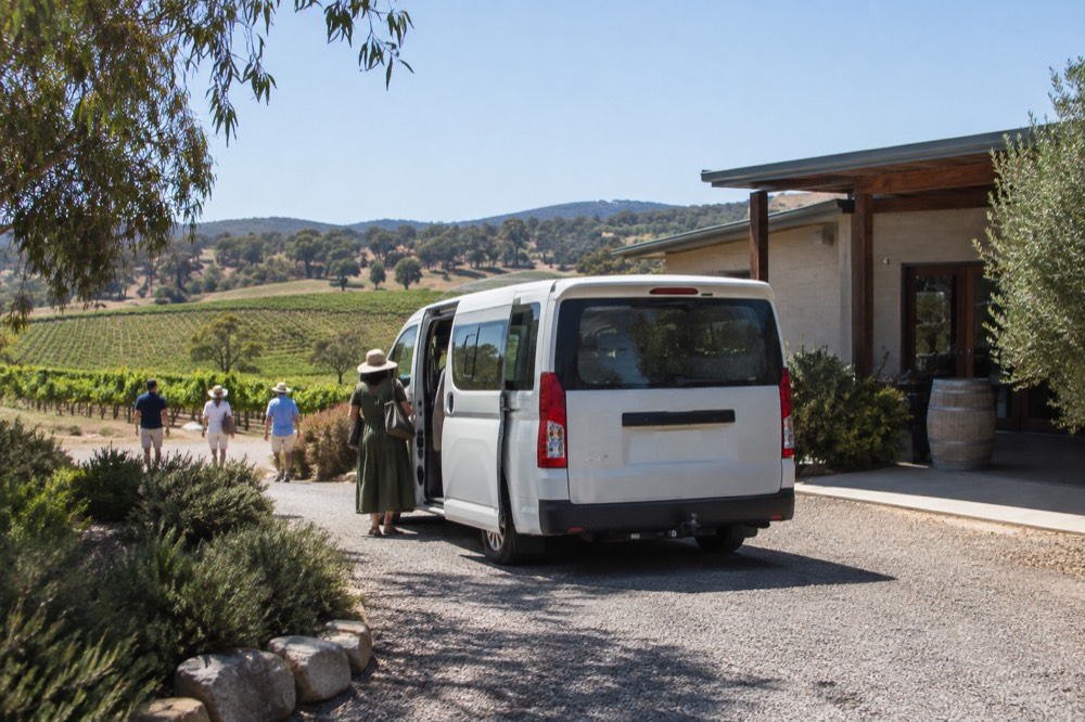 A small tour van parked on a gravel driveway beside a winery building