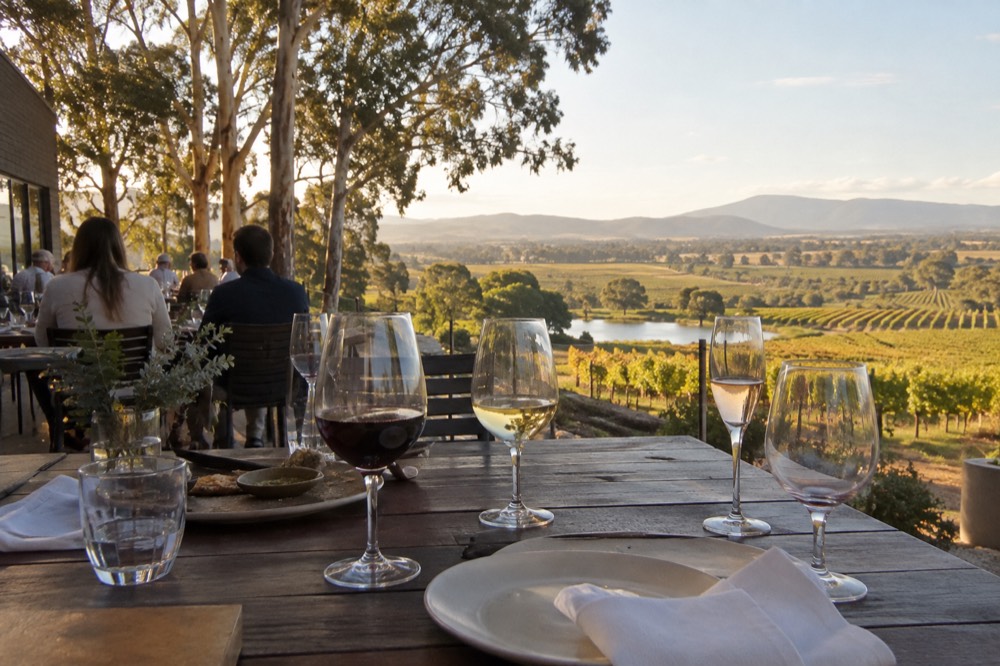 A group of wine glasses on an outdoor table overlooking vineyards in late afternoon light