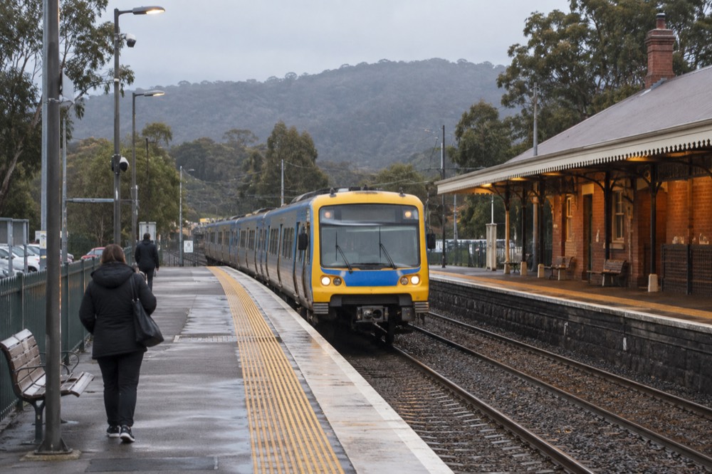 A metro train arriving at an outer suburban station platform with hills in the distance