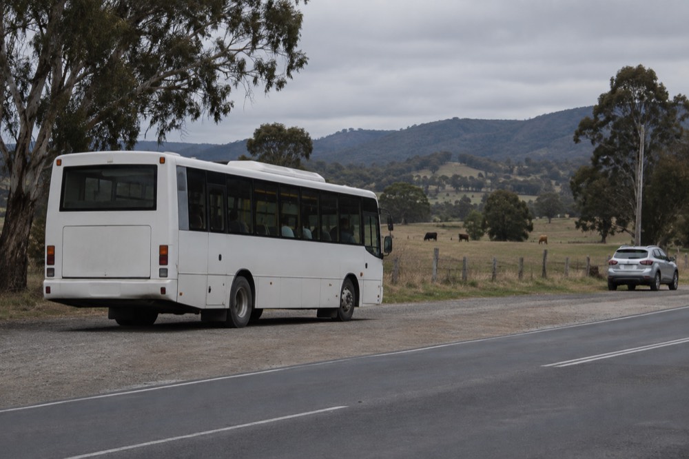 A regional route bus pulled up at a roadside stop beside farmland