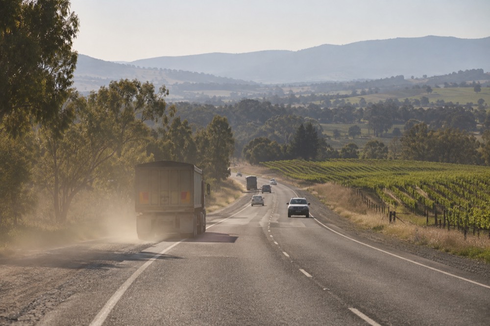 Country highway curving past vineyards with hills on the horizon