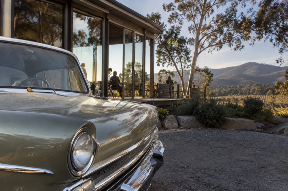 A gleaming vintage car bonnet reflected in the glass of a winery tasting room