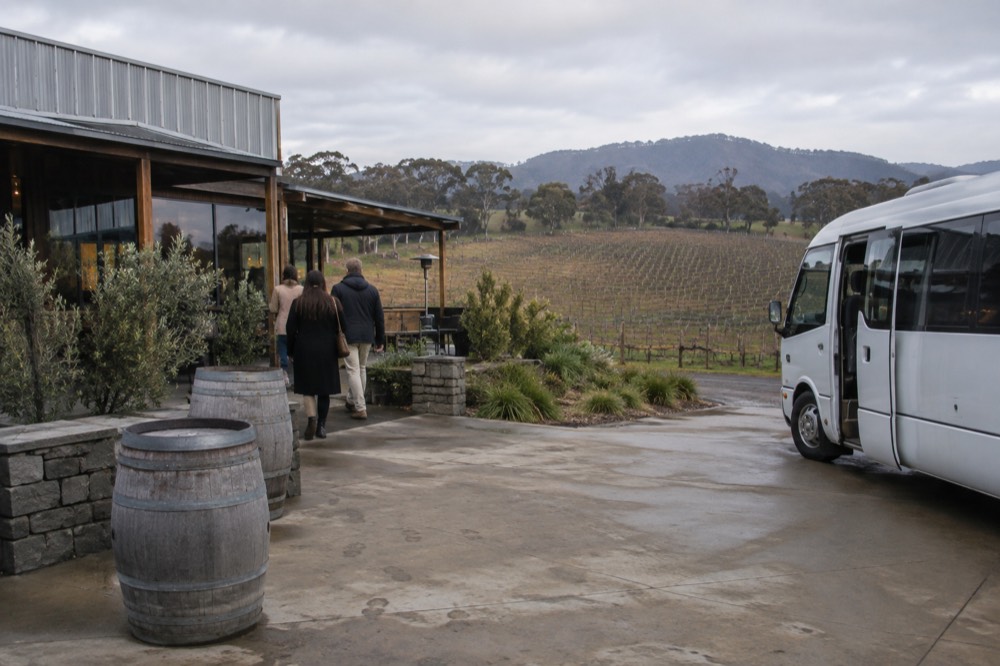 A minibus with its door open at a cellar door entrance framed by bare winter vines