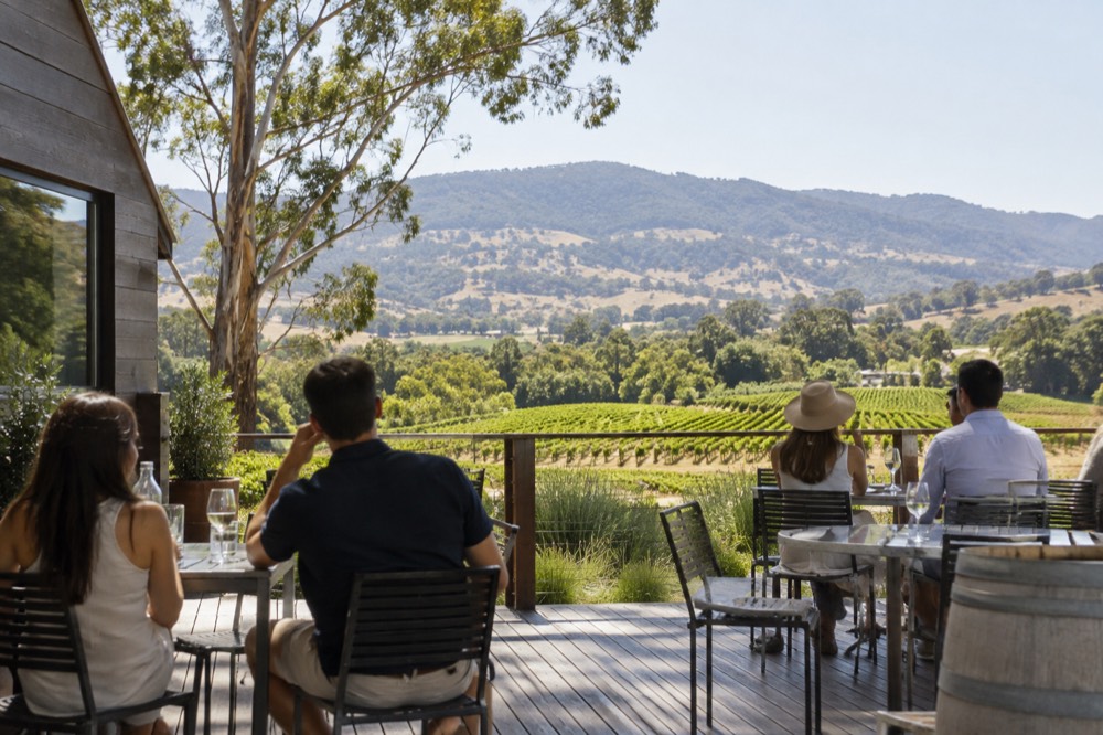Sunlit vineyard terrace with outdoor tables and green hills beyond on a warm day