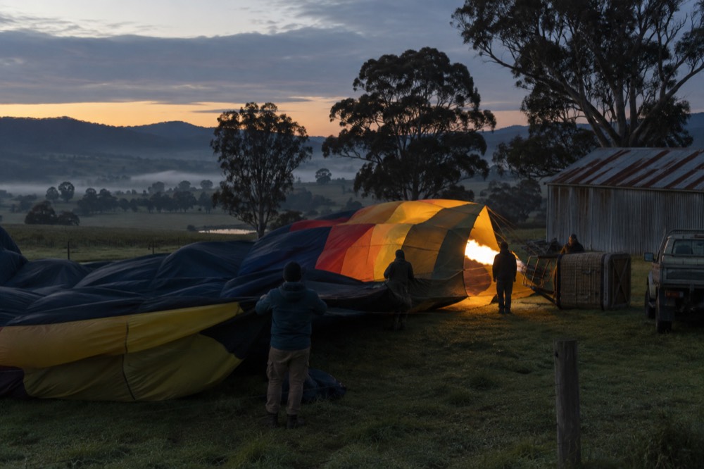 Hot air balloon envelope being inflated in a dark paddock before dawn
