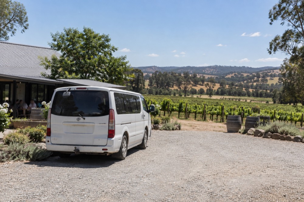 A small tour van parked on a gravel driveway beside a winery building