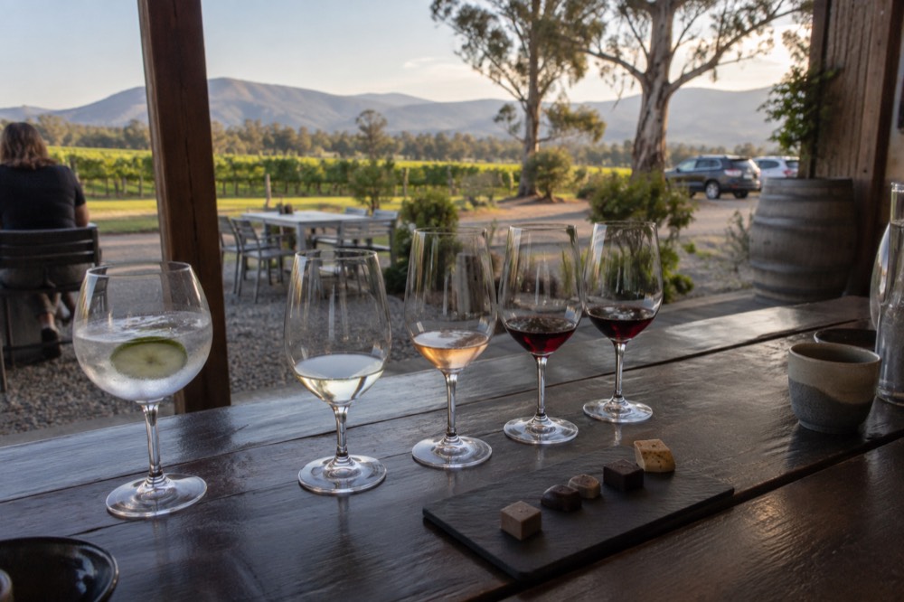 A wooden tasting bench with wine glasses, a gin glass and a plate of chocolates arranged in a row