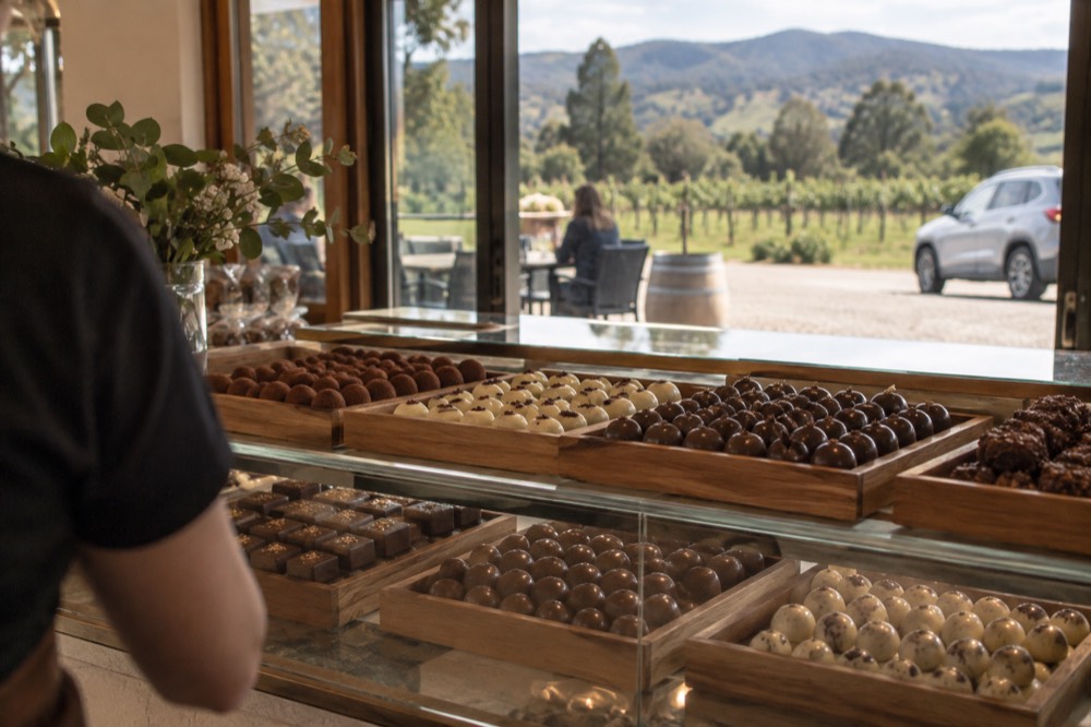 A chocolate shop counter with trays of handmade chocolates behind glass