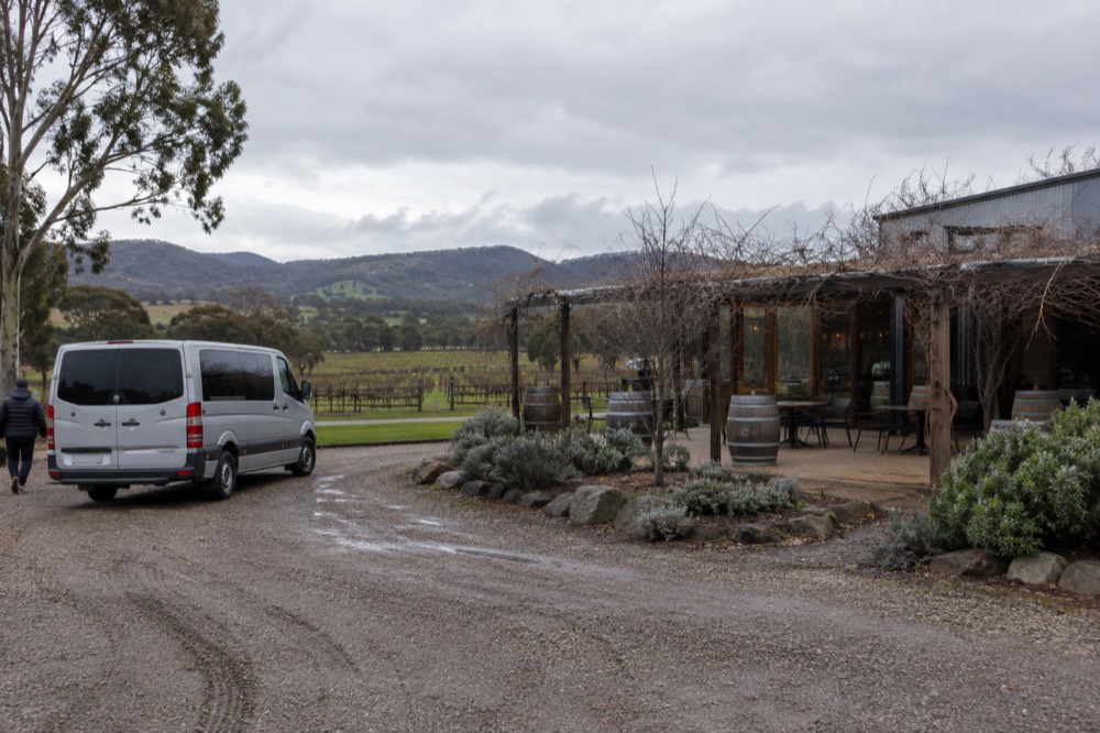 A small van parked on a gravel driveway beside a winery cellar door building
