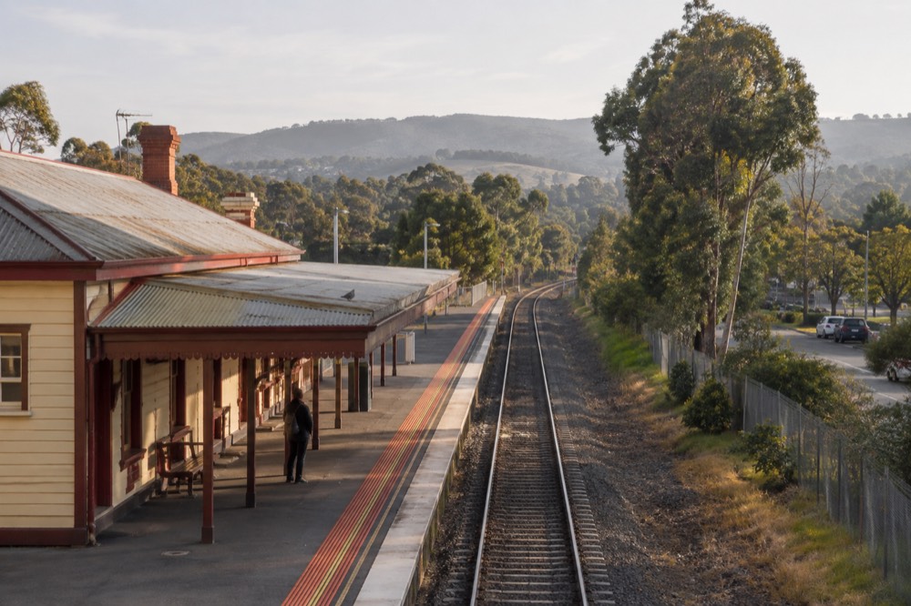 A regional train station platform at Lilydale with tracks running toward distant green hills