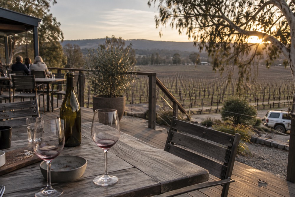 Outdoor tasting table with wine glasses on a timber deck overlooking vines