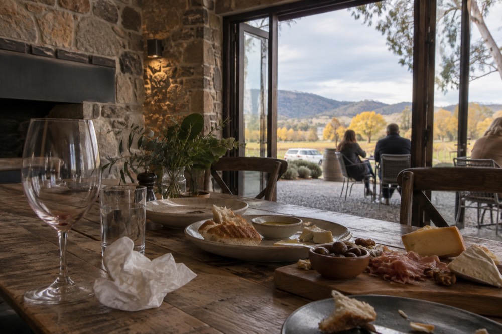 Wooden table laid with shared platters of bread, cheese and charcuterie inside a winery dining room